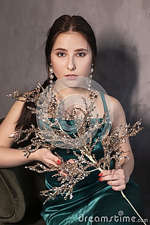 Sexy attractive brunette woman in elegant green aquamarine dress with artificial branch with sparkly sequins. beautiful sensual Stock Photo