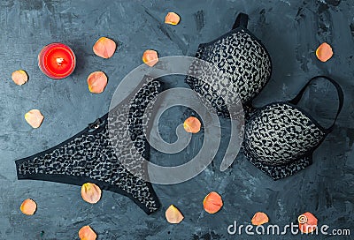 Sexy black set of a bra and thong on black wooden background with a candle and coral rose leafs , flat lay Stock Photo