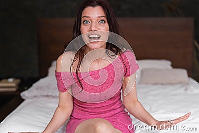 Sexy brunette in a hotel room. Morning awakening and emotions of surprise on the face of a young lady. She sits on the Stock Photo