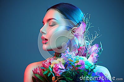 Sexy brunette model girl with bouquet of beautiful flowers. Beauty young woman with bunch of flowers in colorful neon lights Stock Photo