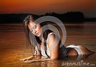 brunette woman in lingerie laying in river water. Young female relaxing on the beach during sunset. Perfect body girl Stock Photo