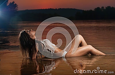 brunette woman in lingerie laying in river water. Young female relaxing on the beach during sunset. Perfect body girl Stock Photo