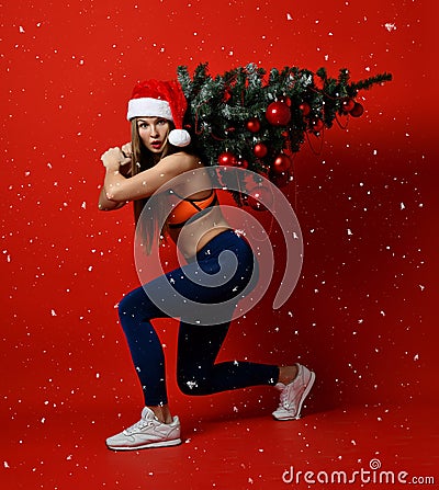 Christmas fitness sport woman wearing santa hat holding xmas tree on her shoulders. snowflakes Stock Photo