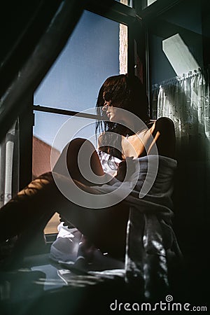 Sexy girl in a Bathrobe sitting on the windowsill Stock Photo