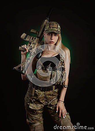 A sexy girl in military airsoft overalls poses with a gun in her hands on a dark background Stock Photo