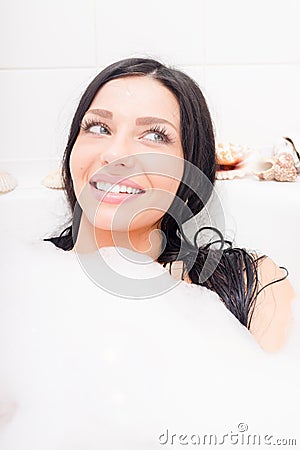 seductive young brunette blue eyes woman lying relaxing in the bath with foam happy smiling & looking aside closeup portrait Stock Photo