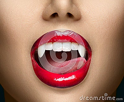 Sexy Vampire Woman`s red bloody lips close-up. Vampire girl licking fangs with tongue. Fashion Glamour Halloween Stock Photo