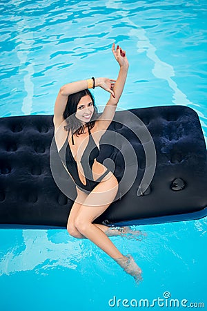 woman in black bikini sitting on an inflatable mattress in swimming pool and looking to the camera Stock Photo