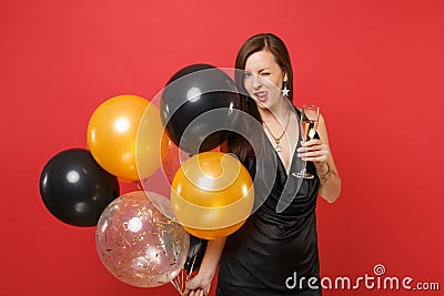 woman in black dress celebrating blinking licking lips, holding glass of champagne, air balloons isolated on red Stock Photo