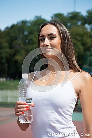 woman with plastic bottle on stadium. Woman with water bottle on sunny outdoor. Drinking water for health. Thirst and dehydra Stock Photo