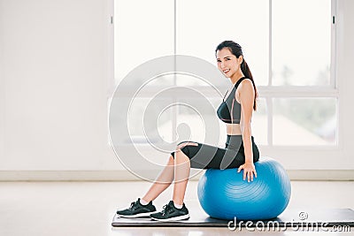 young Asian girl exercise, smile on fitness ball at clean home gym, sports club. Yoga aerobic class, sport trainer Stock Photo