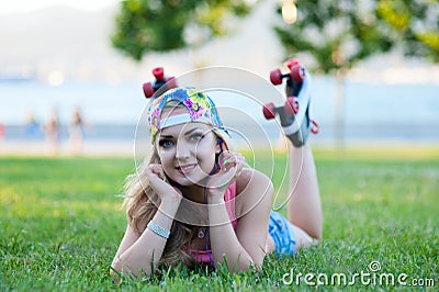 young blond girl in vintage rollers lying on lawn in park and listening to music on headphones Stock Photo