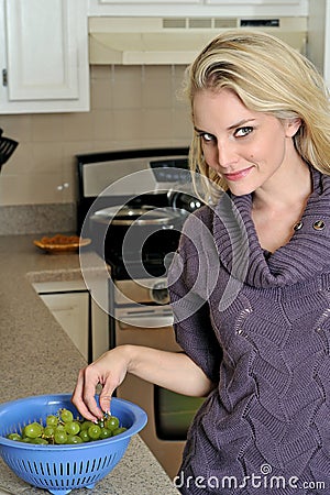 young blonde woman washing grapes in kitchen Stock Photo