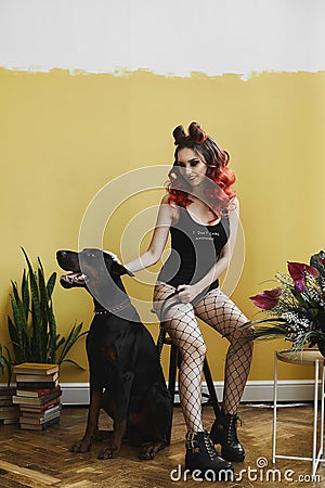 Sexy young model woman with red hair and with perfect body in black stylish bodysuits and in mesh pantyhose sits on the Stock Photo