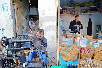 A cobbler at work inside the medina with a sewing machine and stalls of nuts on the right side Editorial Stock Photo