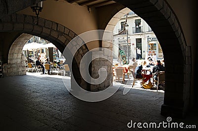 From the shade of a medieval arcaded pavement, a view to a busy, vibrant street in the old Catalan city of Girona, Spain. Bulky Editorial Stock Photo