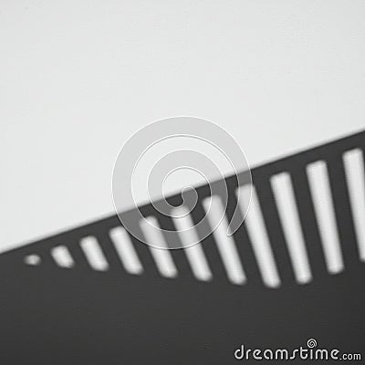 A shadow is cast on a light surface at an angle, creating alternating patterns of light and Stock Photo