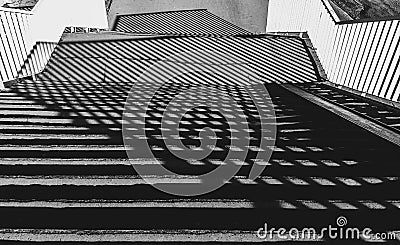 The shadow cast by the railing creates symmetrical patterns on the stairs. Black and white Stock Photo