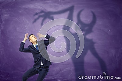 Shadow of devil trying to catch the frightened businessman Stock Photo
