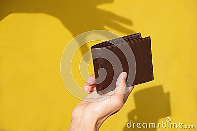 Shadow of robbers hand on yellow wall trying to steal leather wallet from persons hand. Pickpocket silhouette. Concept of Stock Photo