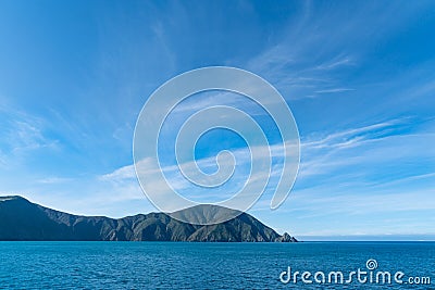 Shadows on hills under blue sky with light wispy cloud entering Queen Charlotte Sound Stock Photo