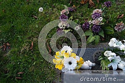 Shallow, abstract focus of artificial flowers seen at the base of a granite gravestone. Stock Photo