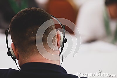 Shallow depth of field selective focus image with a man sitting on a chair and listening to a conference and having headphones Editorial Stock Photo
