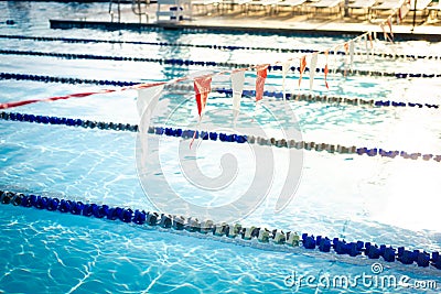 Shallow DOF string of colorful triangular backstroke flags hanging over public competitive swimming pool with pool lane divider Stock Photo