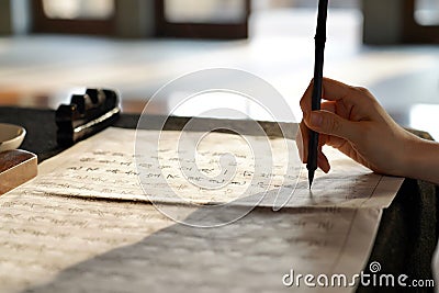 Shallow focus of a person's hand holding a traditional Chinese brush above the papers with writings Editorial Stock Photo