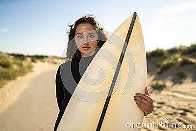 Shallow focus shot of an attractive female holding a surfboard in the middle of the road in Spain Stock Photo