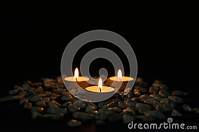 Shallow focus shot of three lit candles in stones and pebbles in front of a black background Stock Photo