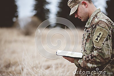 Shallow focus shot of a young soldier reading a bible in a field Stock Photo