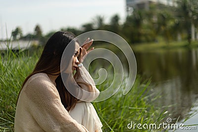 Shallow focus on a thoughtful Asian woman sitting in the grass and looking ahead Stock Photo