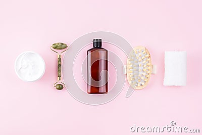 Shampoo or cosmetic lotion bottle, jade roller, towel, open cream jar, massager. Skin care products on pink surface Stock Photo