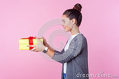 Share present. Side view portrait of generous teenage brunette girl giving gift box. pink background Stock Photo