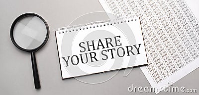 Share your story sign in white paper notepad and magnifying glass on the grey background Stock Photo