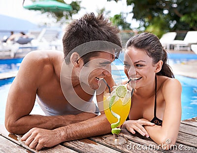 Sharing a drink. an attractive young couple sharing a cocktail on the edge of a pool. Stock Photo