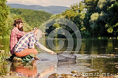 Sharing his secrets. Friends spend nice time at riverside. Beautiful evening riverside. Experienced fisherman show tips Stock Photo