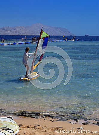 Sharm el-Sheikh, Egypt - March 14, 2018. A girl runs a board with a sail on the mast due to the inclination and turn of the mast. Editorial Stock Photo