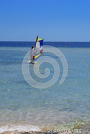 Sharm el-Sheikh, Egypt - March 14, 2018. A girl runs a board with a sail on the mast due to the inclination and turn of the mast. Editorial Stock Photo