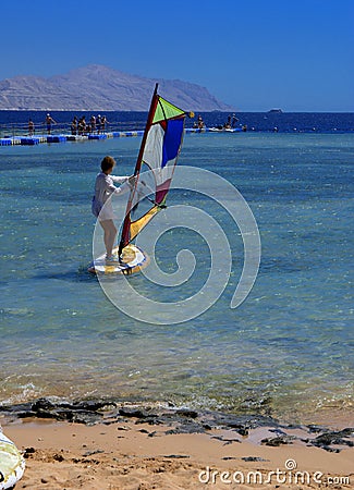Sharm el-Sheikh, Egypt - March 14, 2018. A girl runs a board with a sail on the mast due to the inclination and turn of the mast. Editorial Stock Photo