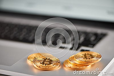 Sharp focus on golden bitcoins placed on silver laptop with blurred financial chart on its screen. Stock Photo