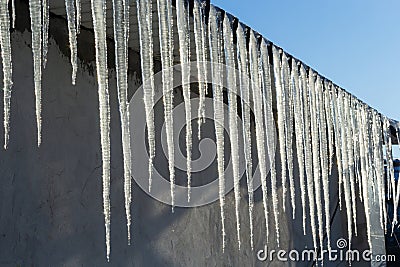 Sharp icicles and melted snow hanging from eaves of roof. Beautiful transparent icicles slowly gliding of a roof Stock Photo