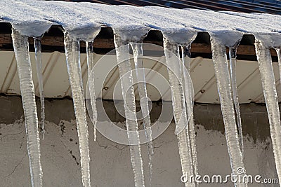 Sharp icicles and melted snow hanging from the eaves of the roof. Beautiful transparent icicles slowly gliding of a roof Stock Photo