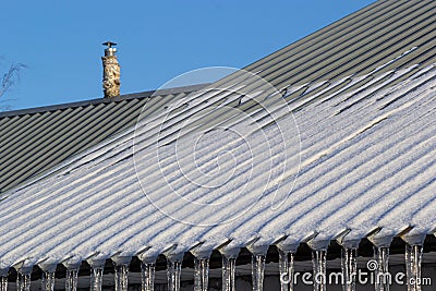 Sharp icicles and melted snow hanging from eaves of roof. Beautiful transparent icicles slowly gliding of a roof Stock Photo