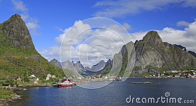 Sharp mountains, red huts and fishing boats reflected into the fjord in Reine Stock Photo