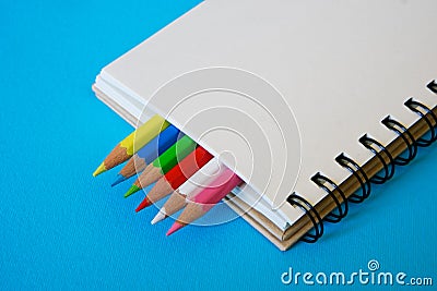 Sharpened colored pencils lie together with a blank notepad on a blue background Stock Photo