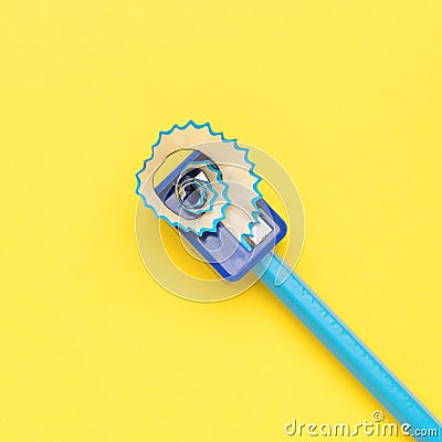 Sharpening a blue pencil with a hand sharpener on a yellow background Stock Photo