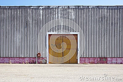The sheet metal factory wall with the entrance door in the industrial park.The red door of the factory building. Stock Photo