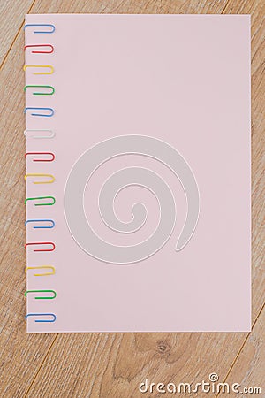 A sheet of pink paper fixed with multi-colored paper clips on the oak plank table close, the Board of the table is located Stock Photo